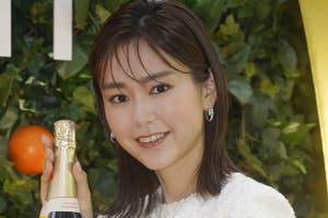 女性がシャンドンのボトルを持って微笑んでいる。白い服を着ている。背景に緑の葉とオレンジがある。
