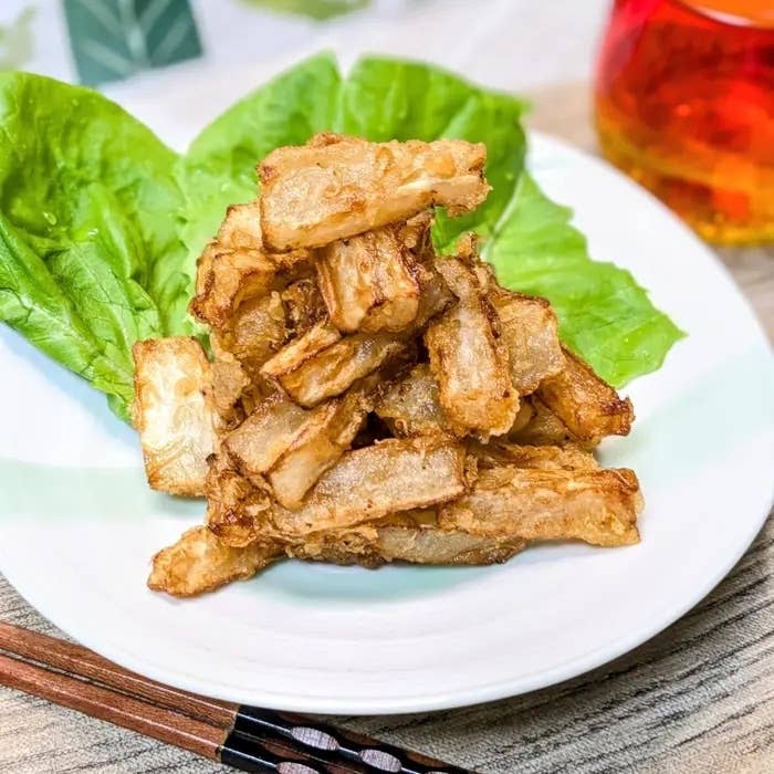 お皿に盛り付けられたフライド根菜の料理。背景にレタスの葉と飲み物があります。