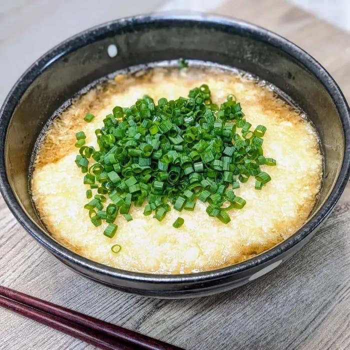 おわんに入ったとろろとじうどん、ネギがトッピングされています。シンプルでおいしそうな和食料理の一例です。