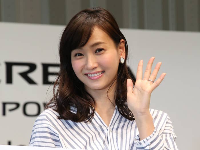 女性が微笑んで手を振っている。ストライプ柄のシャツを着用。