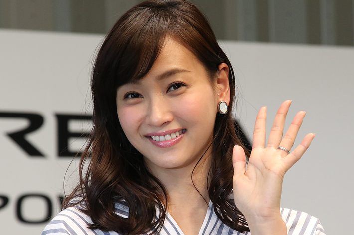 女性が微笑んで手を振っている。ストライプ柄のシャツを着用。