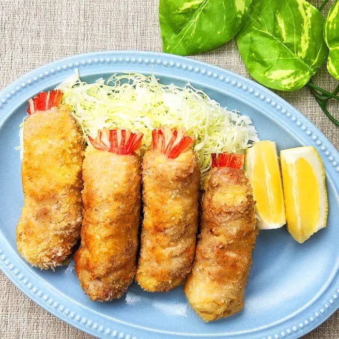 じゃがいもと豚バラ肉でできたエビフライのような揚げ物4本とキャベツ、レモンのスライス。