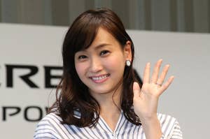 女性がストライプ柄のシャツを着て手を振っている。