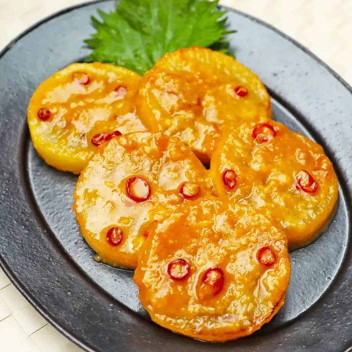 お皿に盛られたピリ辛味の大根のスライス料理。添えられた葉がアクセントになっている。