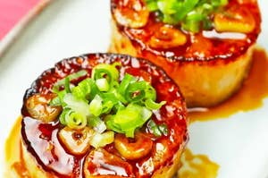 焼き目のついた2つの大根ステーキが、ソースとネギで飾られた皿に盛り付けられている。