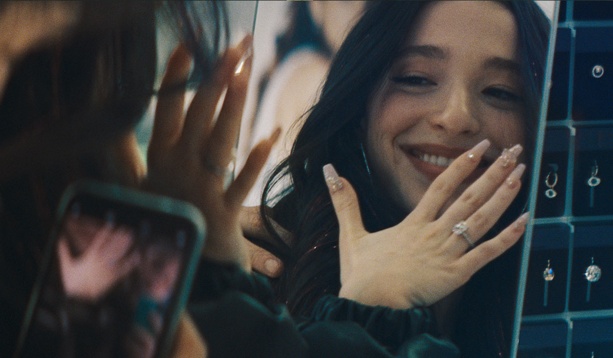 Woman smiling, showing a ring on her hand in a jewelry store, reflected in a mirror