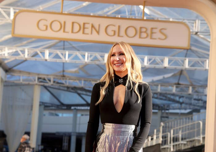 Nikki Glaser on red carpet at Golden Globes wearing a long-sleeve black top with a deep V-neck and a shiny silver skirt
