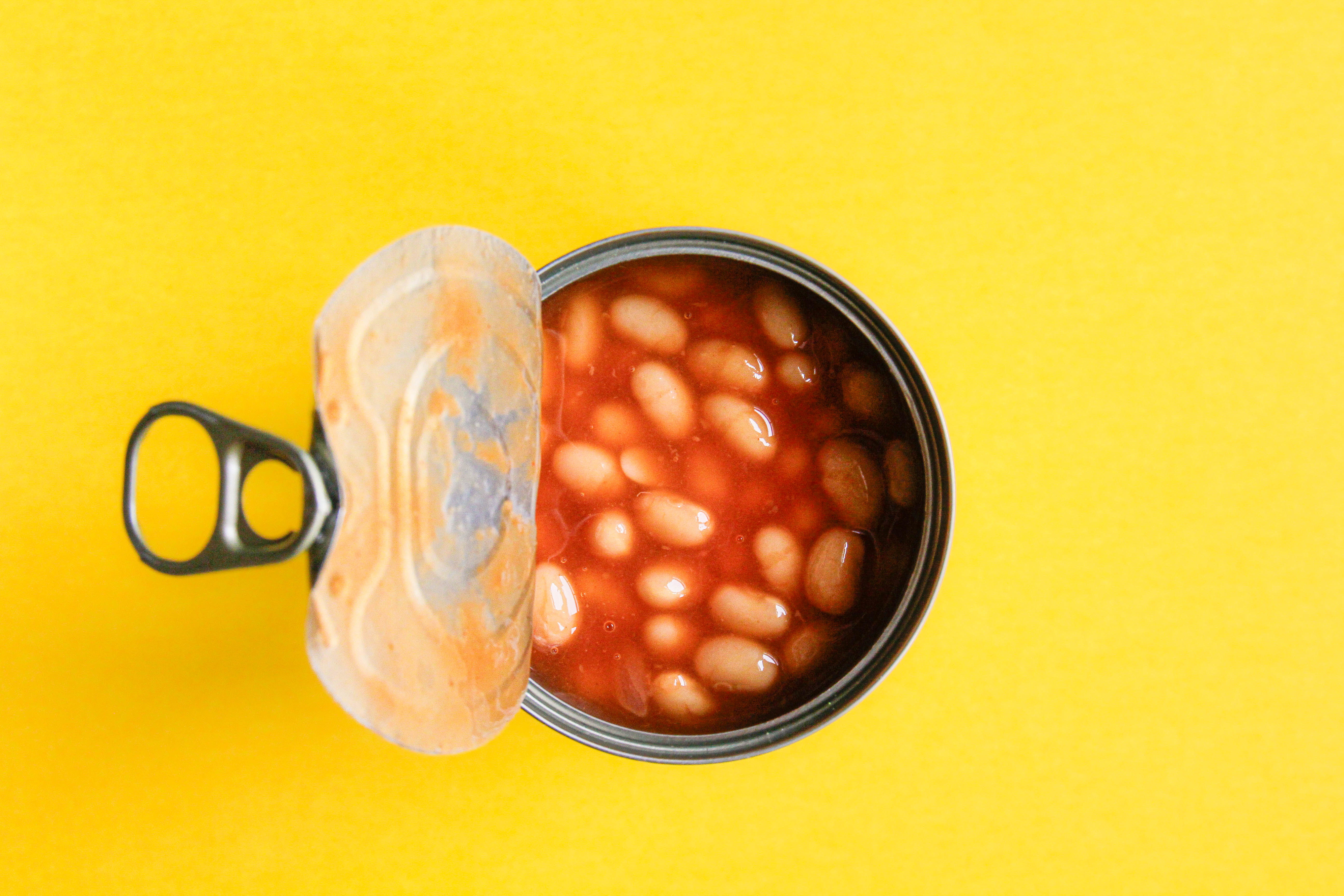 An open can of baked beans with a pull tab against a plain background