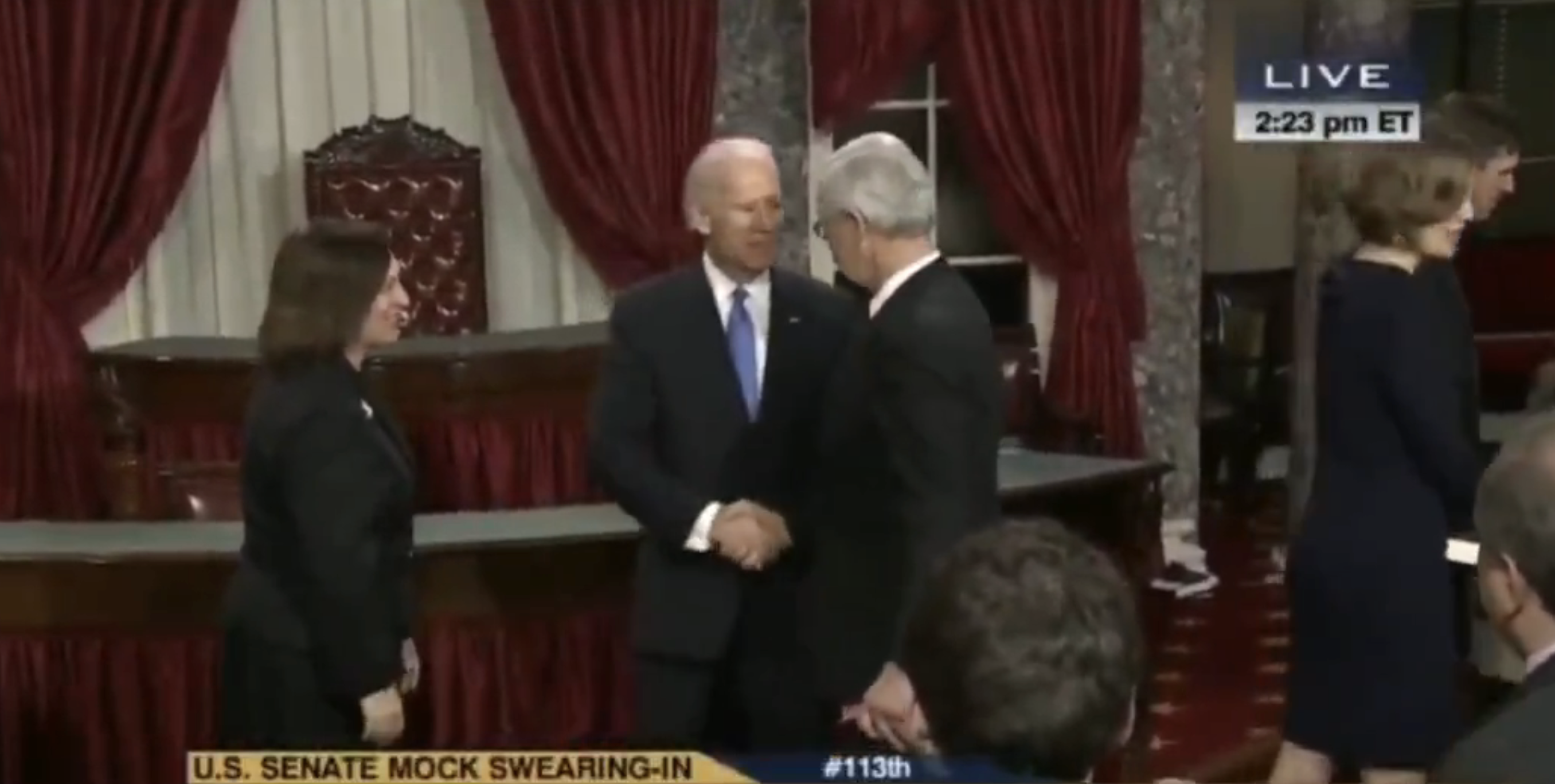 A man in a suit shakes hands with another man during a U.S. Senate mock swearing-in event. Several people are seen standing nearby