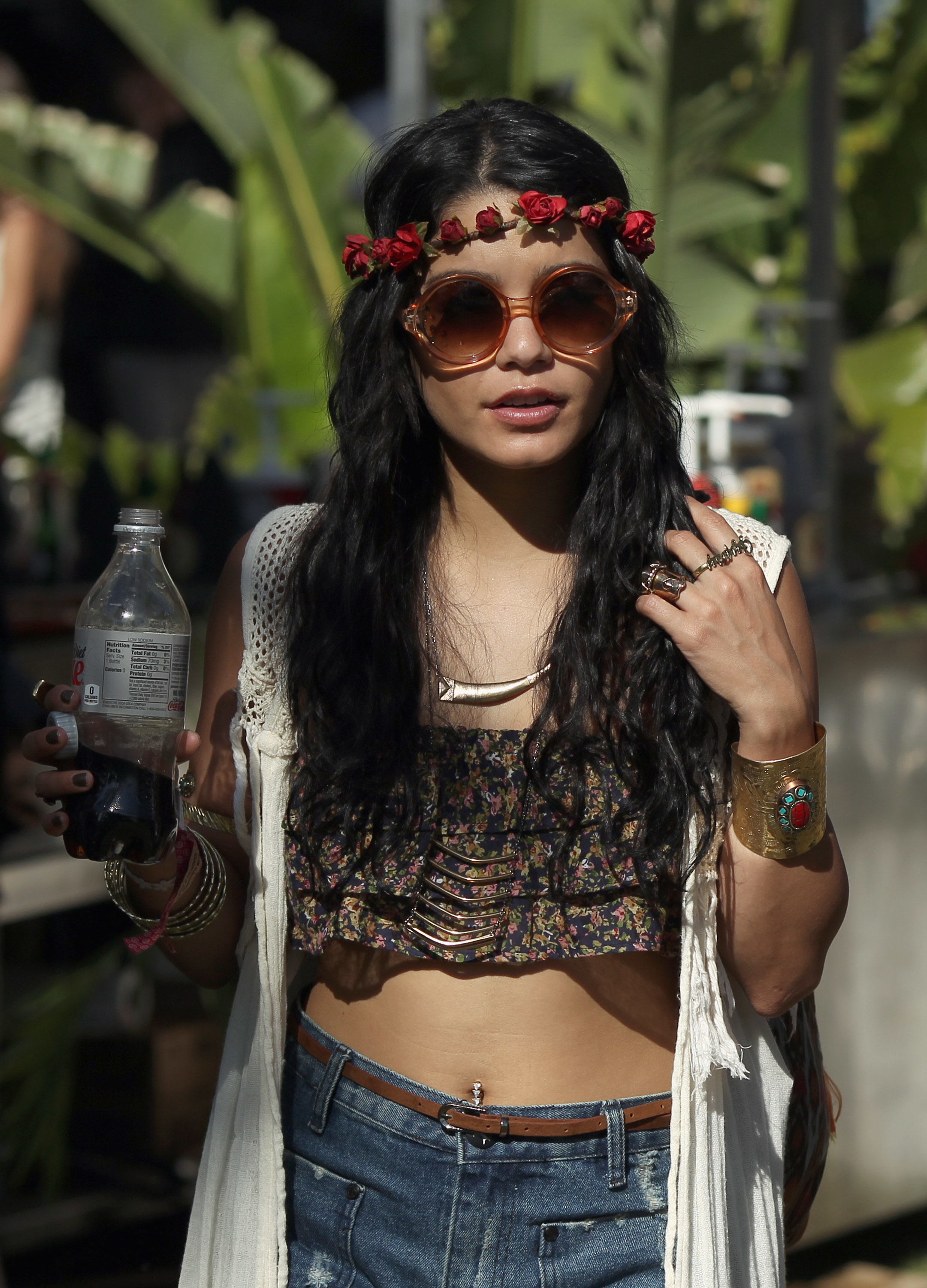 A person in bohemian style: crop top, denim shorts, floral headband, sunglasses, holding a drink