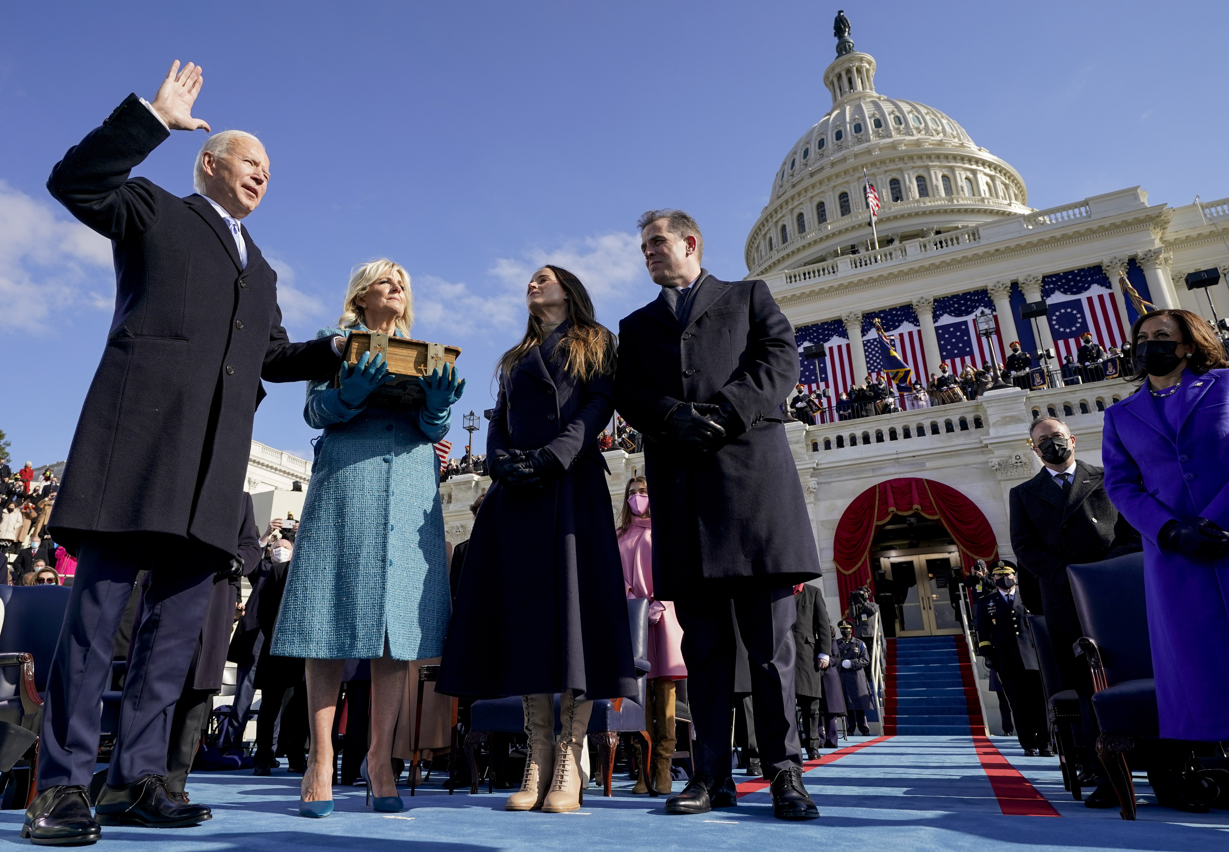 A group stands at a formal ceremony in front of the U.S. Capitol building, with one man raising his hand for an oath. Others wear formal winter attire