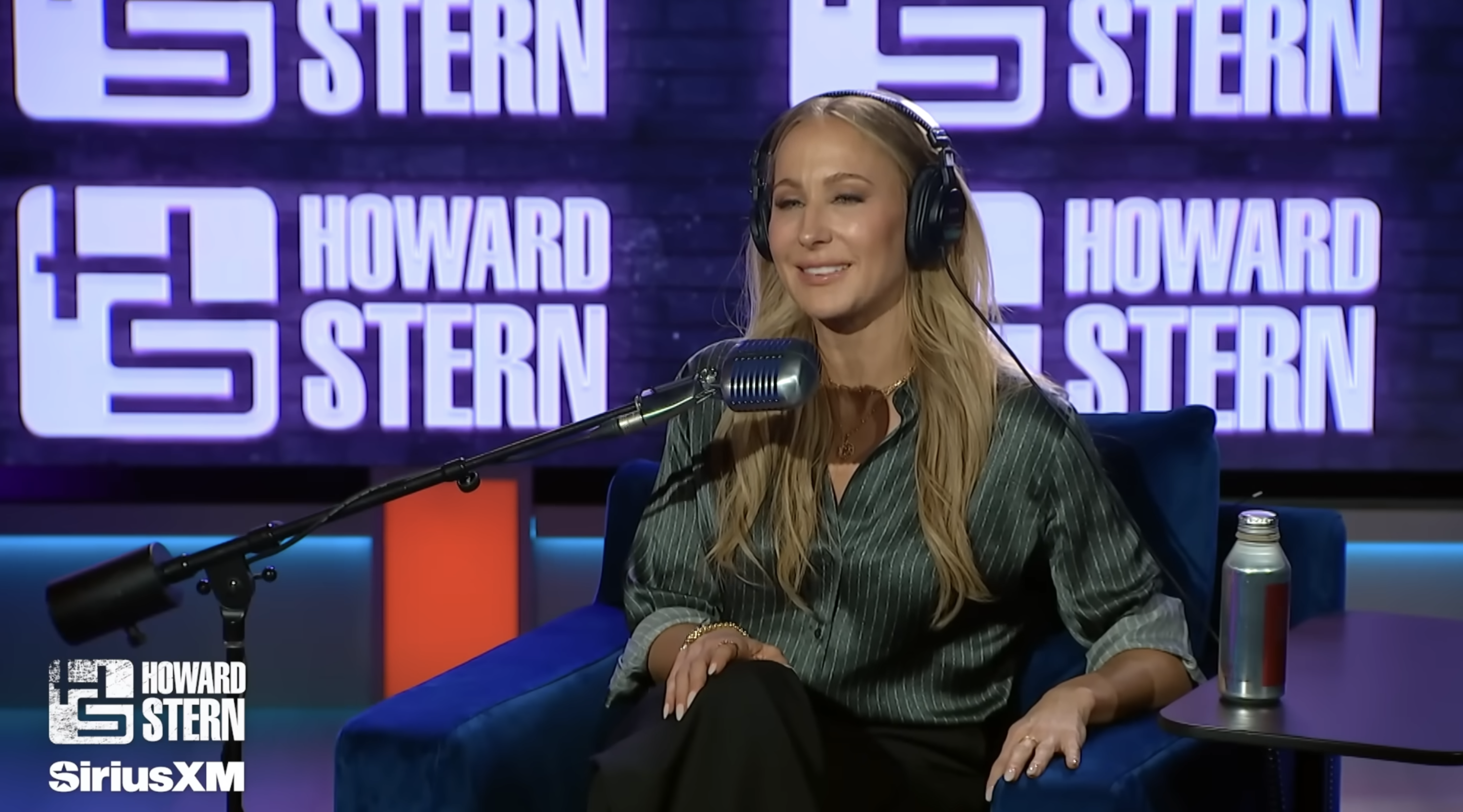 Person in a studio wearing headphones seated at a microphone, with Howard Stern branding in the background