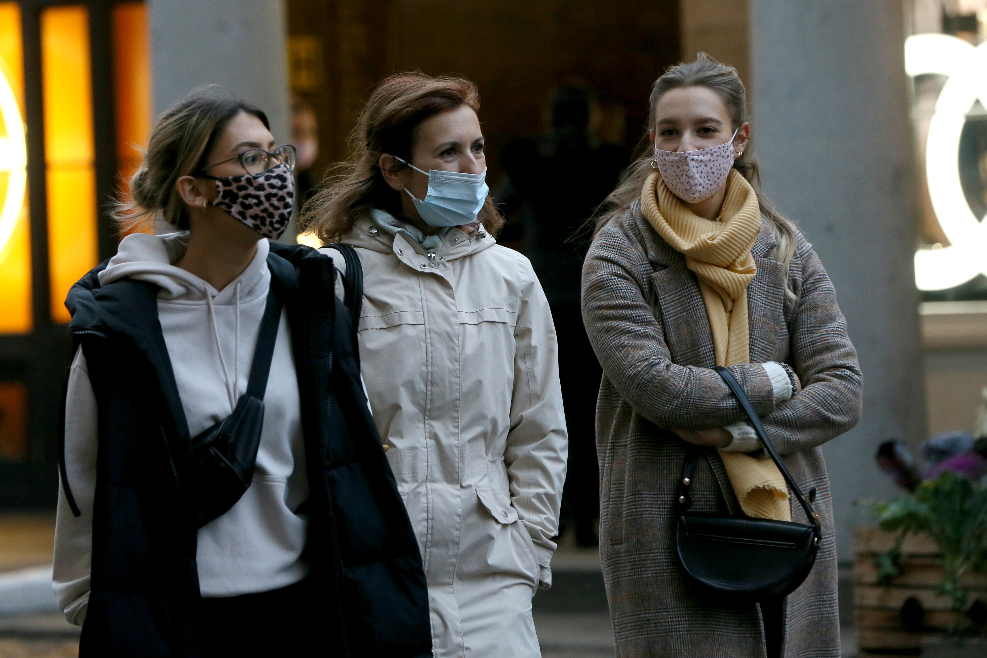 Three women wearing masks and winter clothing walk outside, appearing engaged in conversation