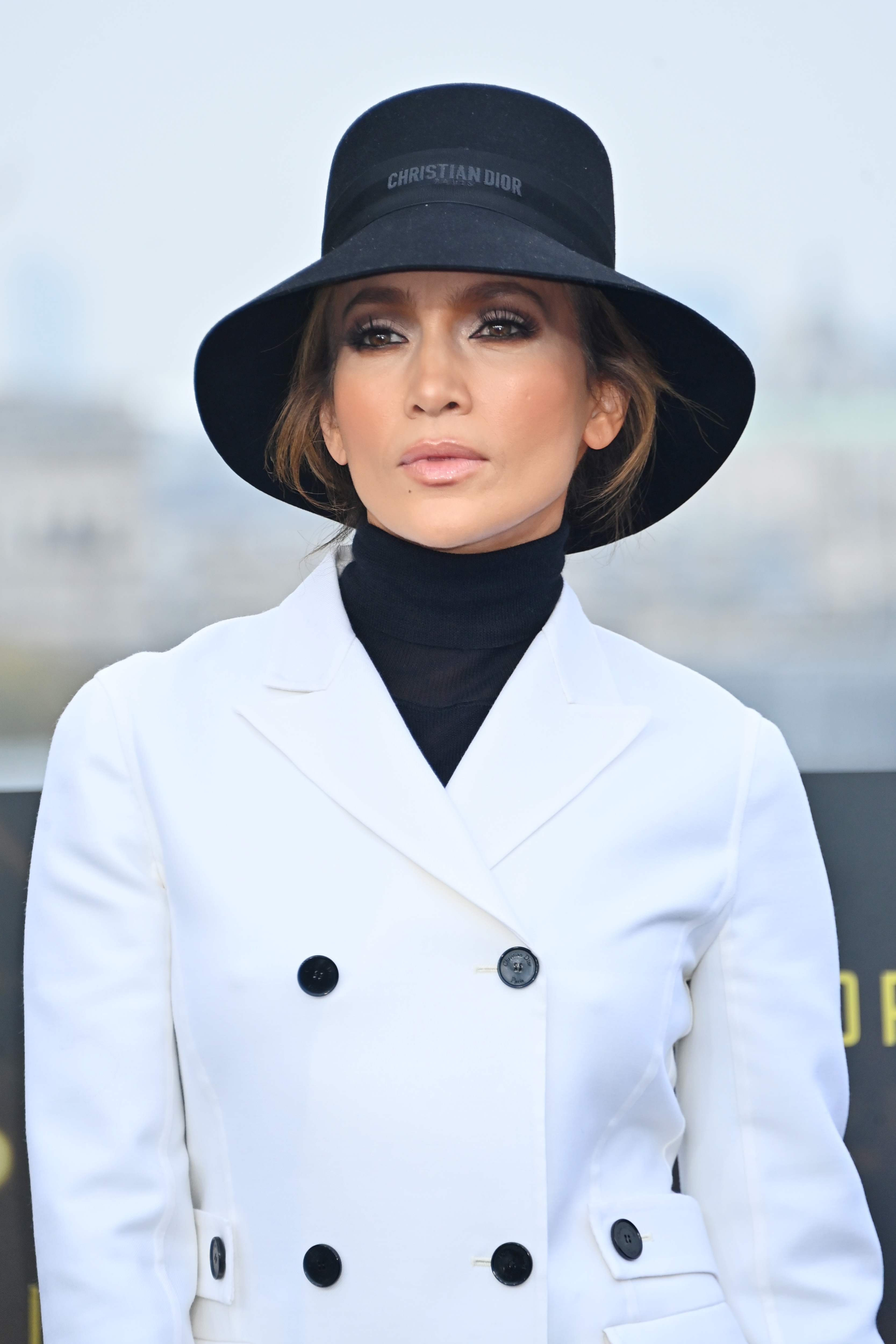 J.Lo in a formal coat and wide-brim hat, outdoors