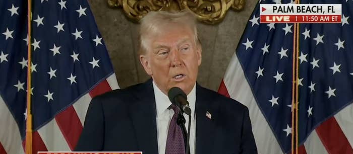 Trump speaks at a podium adorned with US flags during a live news event in Palm Beach, FL