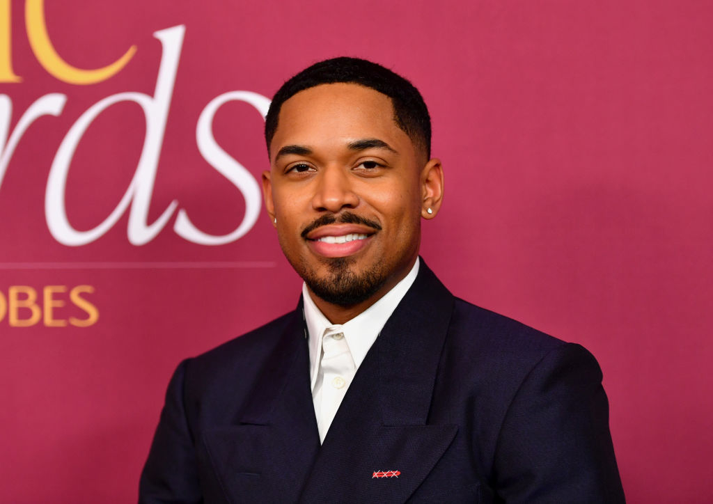 Kelvin Harrison Jr.  in a dark suit with a shirt poses in front of a backdrop with &quot;Awards&quot; partially visible