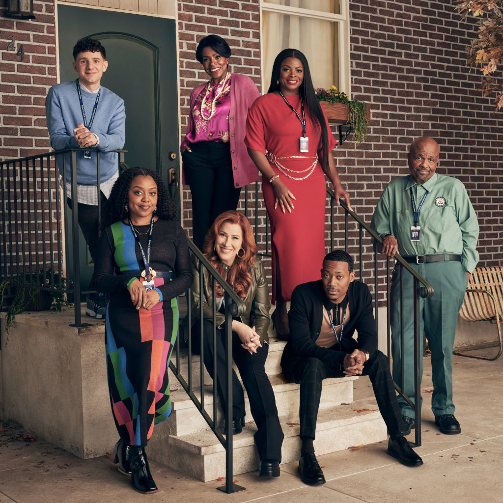 The cast of Abbott Elementary, agroup of seven people, dressed in formal and casual attire, pose on stairs in front of a brick building