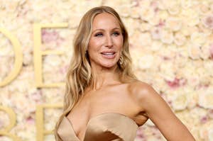 Person on red carpet in strapless gown, smiling, with floral backdrop