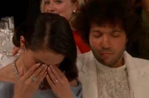 Two people sitting at a formal event; one is wiping their eyes, while the other has a calm expression