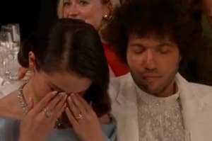 Two people sitting at a formal event; one is wiping their eyes, while the other has a calm expression