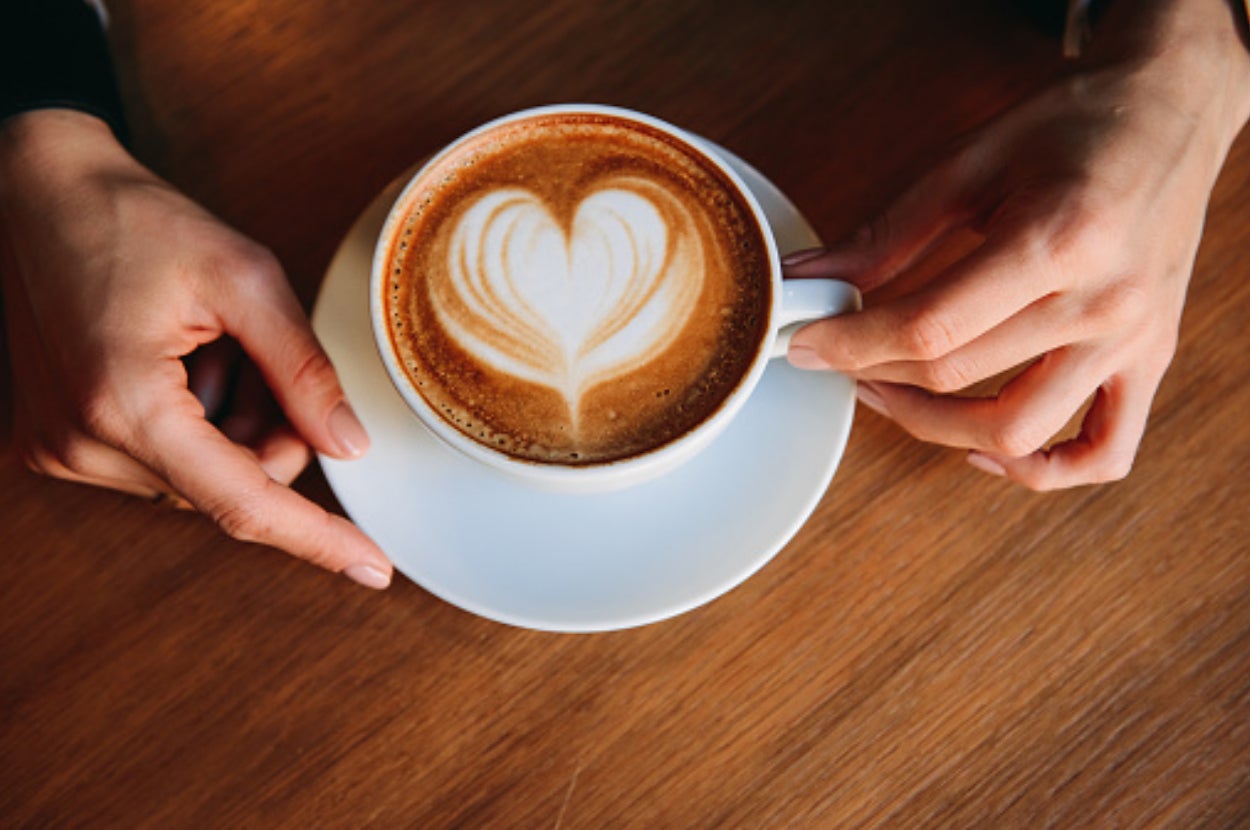 Hands holding a cup of coffee with heart-shaped latte art on a wooden table