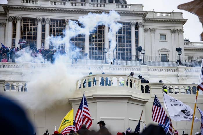 Smoke rises as people gather outside a government building with flags, creating a tense atmosphere