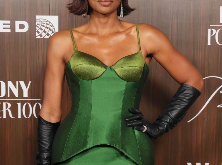 Person posing on a red carpet, wearing an elegant green dress with black gloves, short hair styled softly