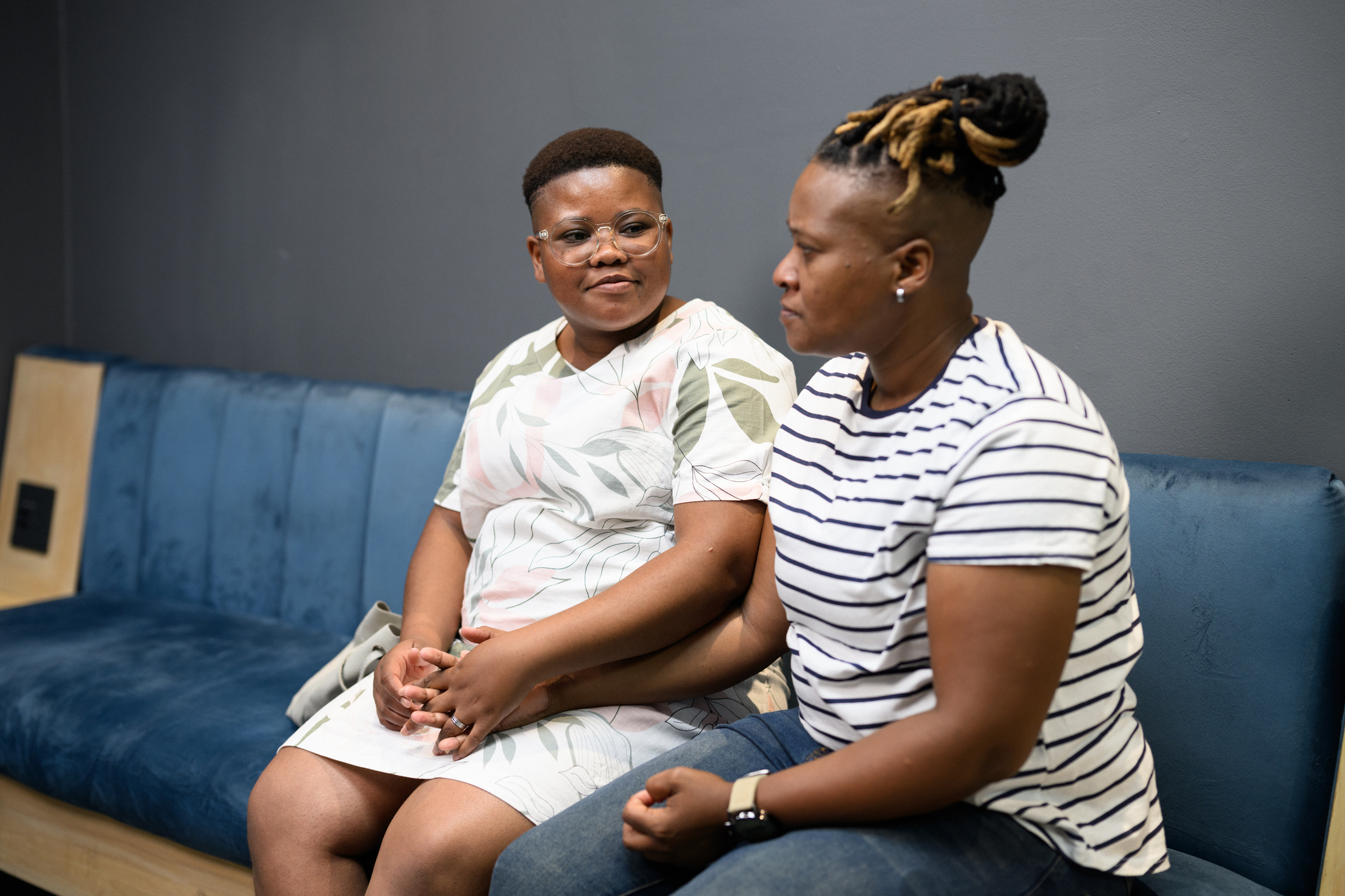 Two people seated on a blue couch, holding hands and looking at each other