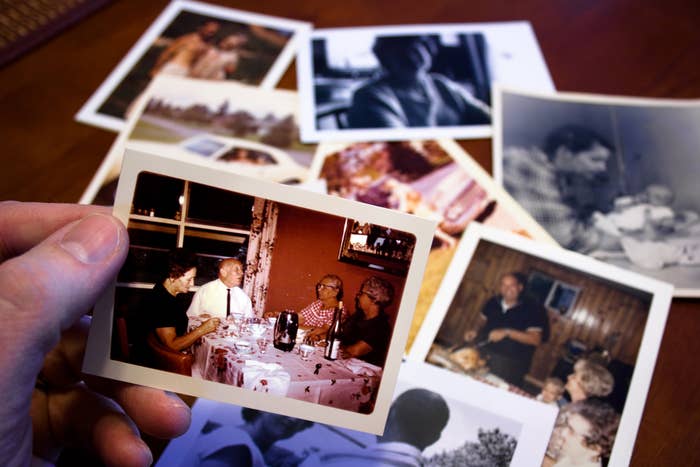 Person holds a family photo at a dining table; other family photos are scattered in the background