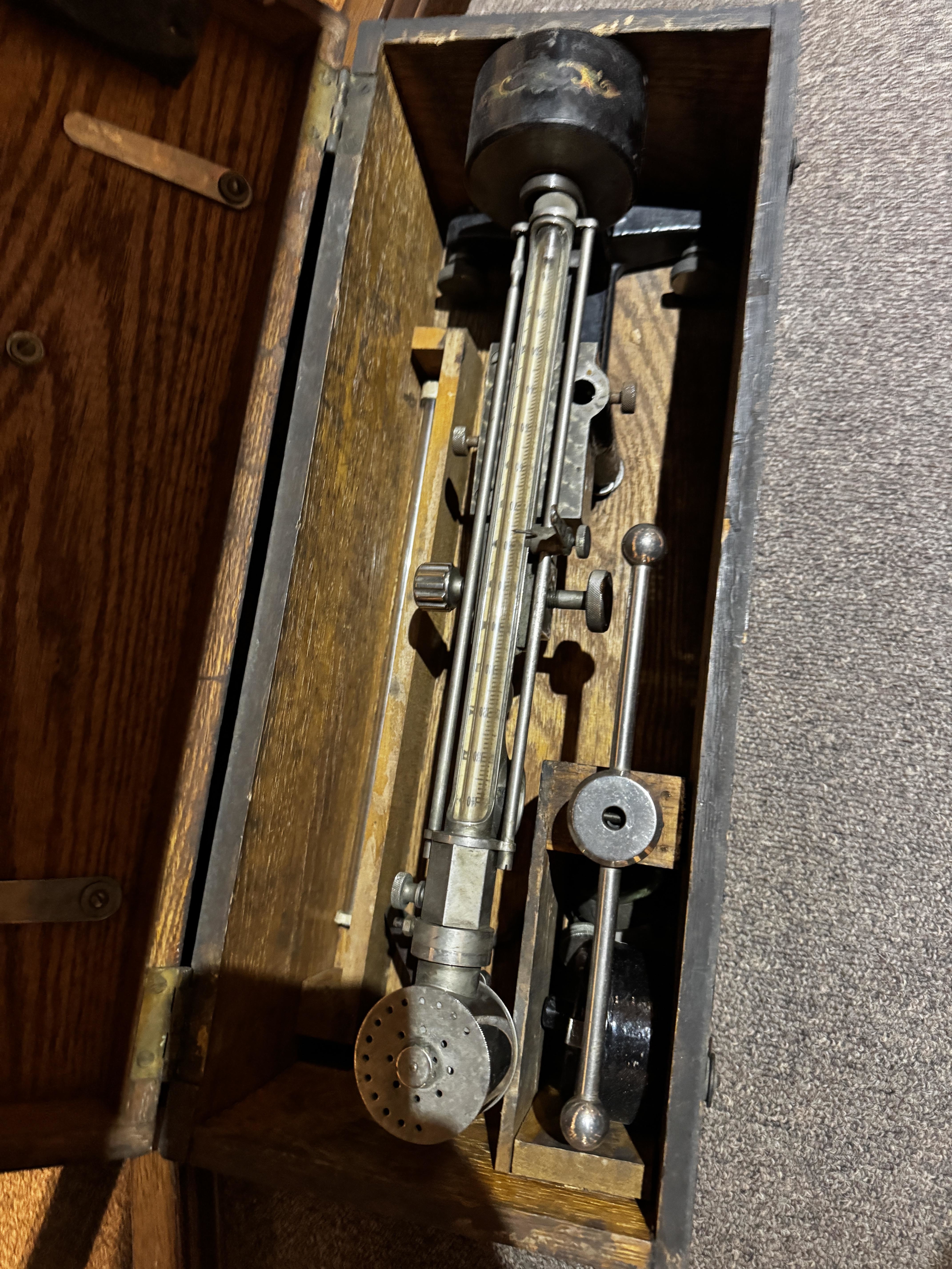 Antique metal and wood apparatus, possibly a scientific instrument, displayed inside a wooden box