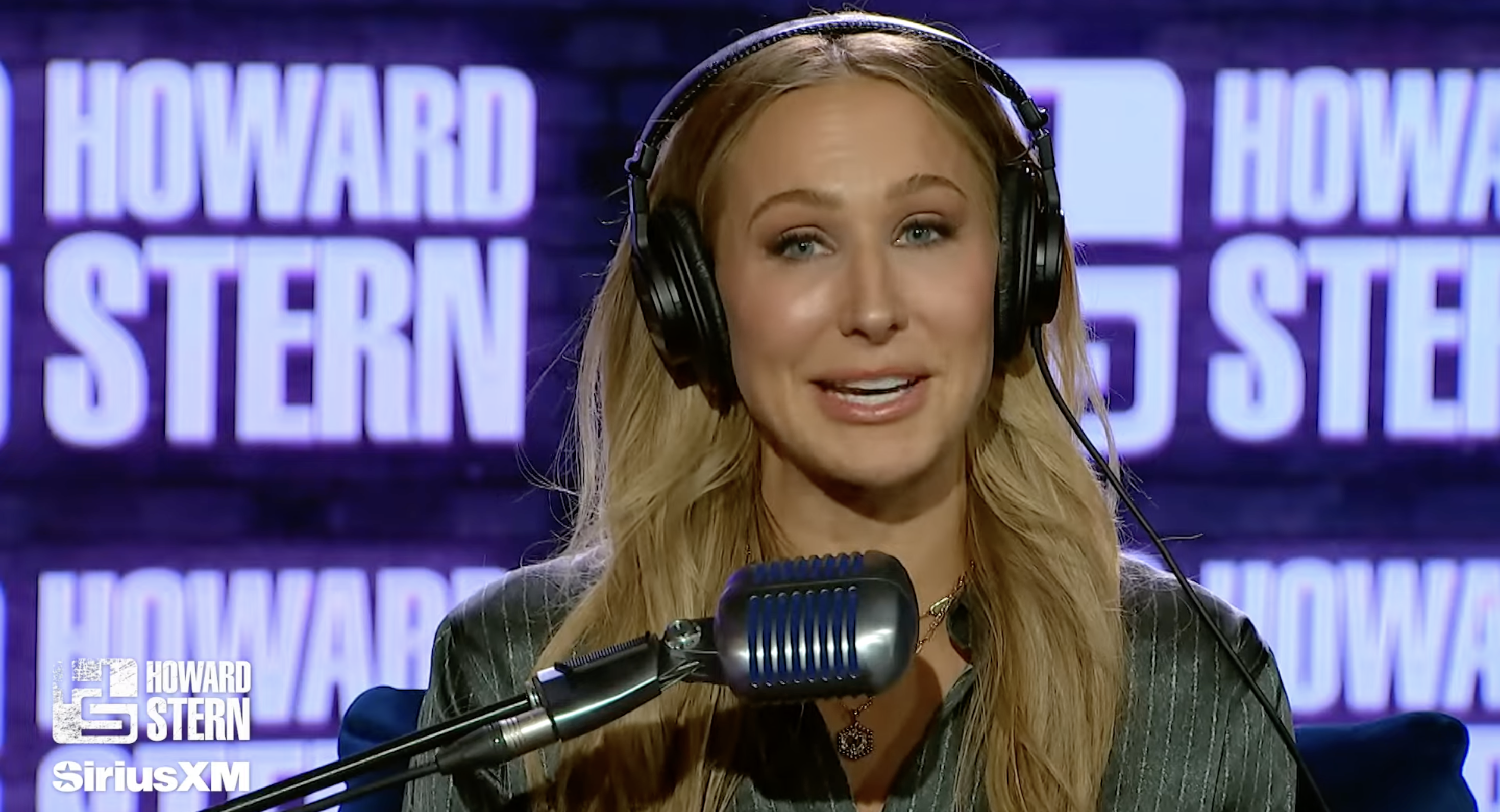 Person wearing headphones speaks into a microphone during a SiriusXM interview. Radio studio setting with Howard Stern branding visible