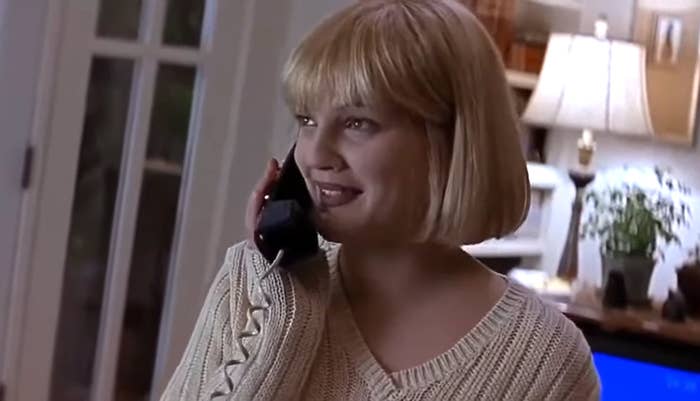 Woman with short blonde hair smiles while talking on a phone, wearing a ribbed sweater indoors