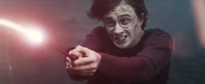 A person in glasses dramatically wields a wand emitting light, suggesting a magical duel scene