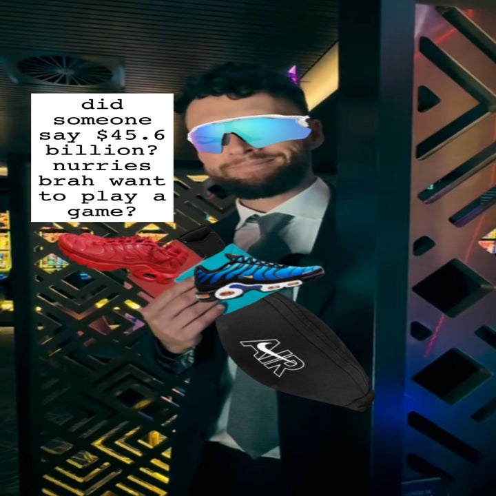 Person in a suit wearing reflective sunglasses, holding two sneakers and an "AIR" branded bag, standing in a modern, patterned background