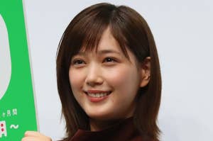 女性が笑顔で看板を持つ。茶色のファッションでシンプルなスタイル。