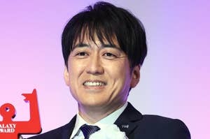 男性がガラシー賞のトロフィーを持って微笑んでいる。スーツを着ていて胸に白い花が付いている。
