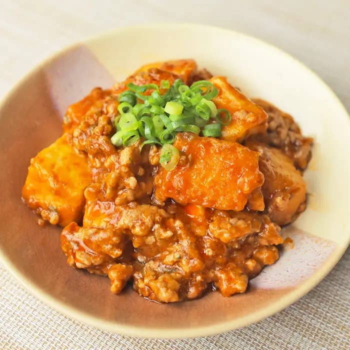 マーボー豆腐が皿に盛られ、上に小ネギがトッピングされている料理の写真。