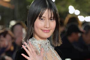 女優が屋外イベントでビジュー付きのゴージャスなドレスを着て、笑顔で手を振っている。背景に観客の姿が見える。