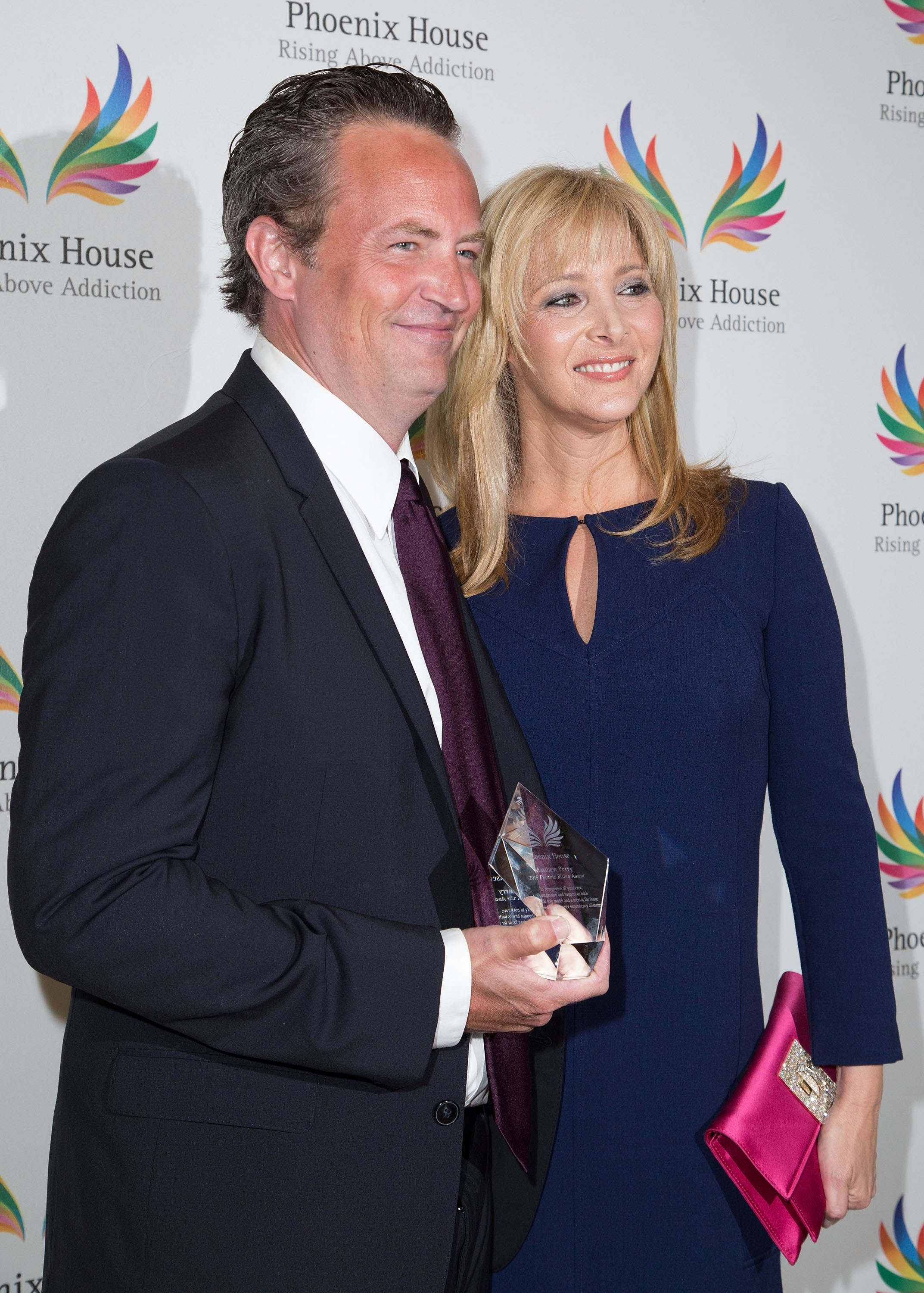 Two people at a Phoenix House event. The man holds an award, wearing a suit. The woman beside him wears a stylish dress and holds a clutch