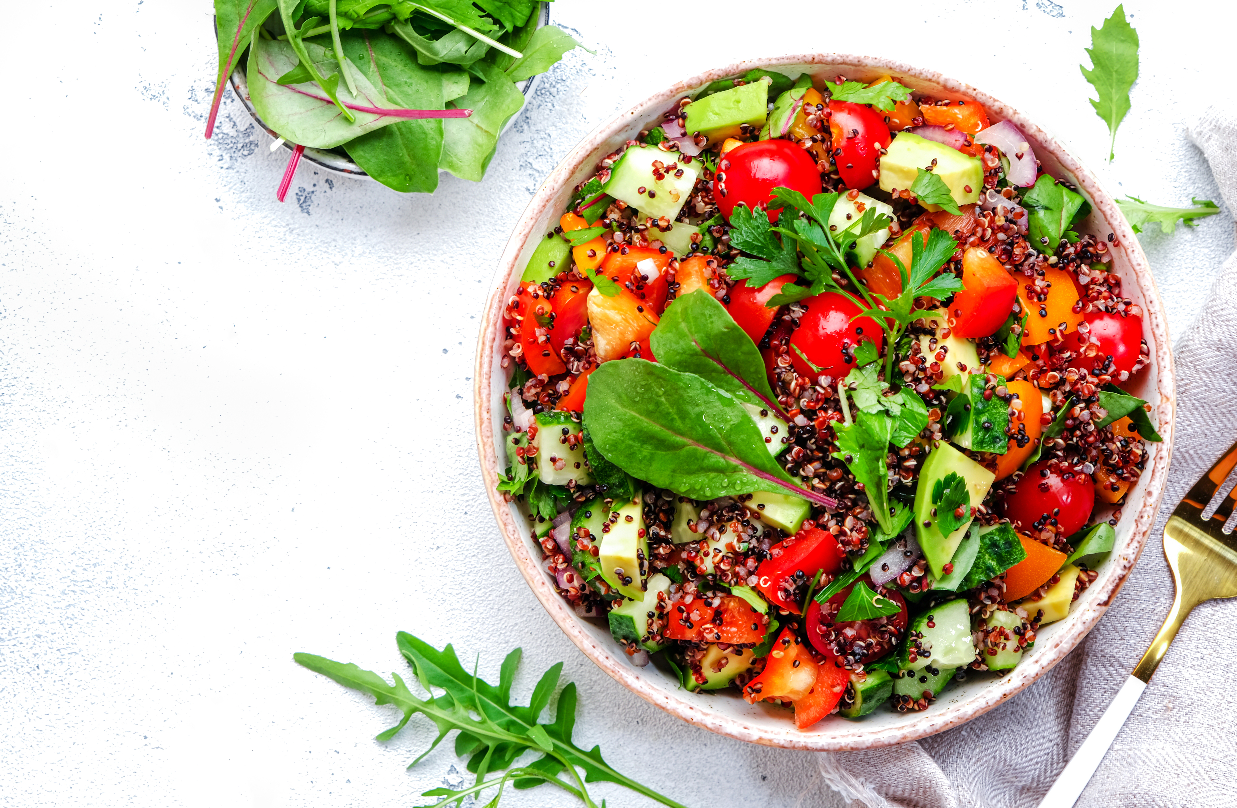 A fresh salad with quinoa, cherry tomatoes, cucumber, bell peppers, and greens in a bowl