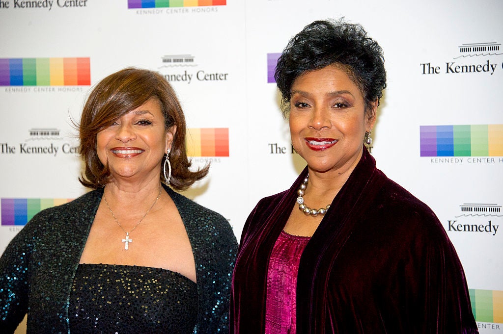 Two women on a Kennedy Center Honors red carpet, both in elegant evening gowns, smiling at the camera