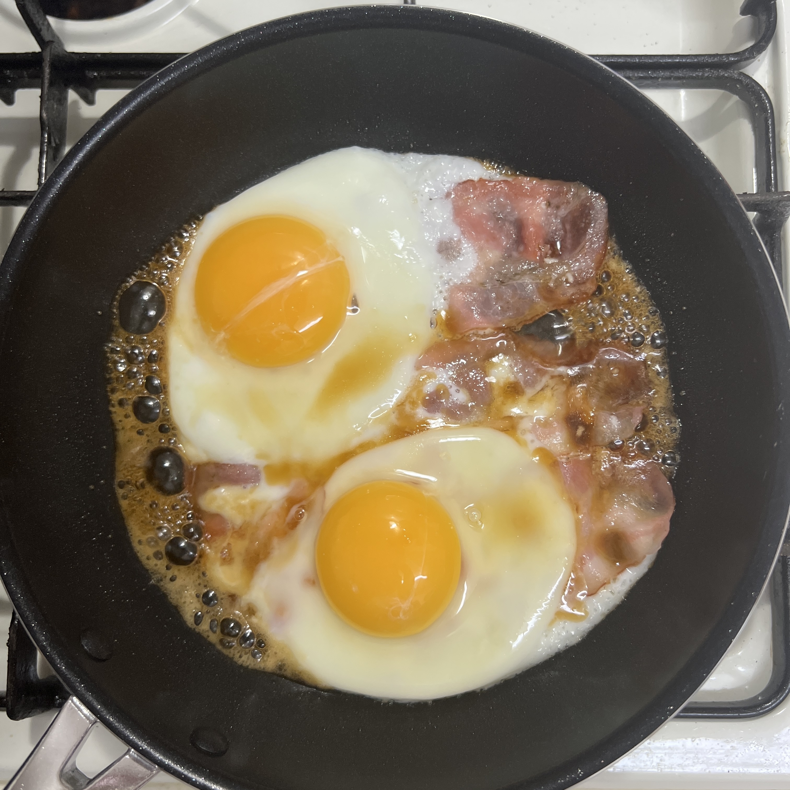 フライパンでベーコンと2つの目玉焼きが焼かれている様子。