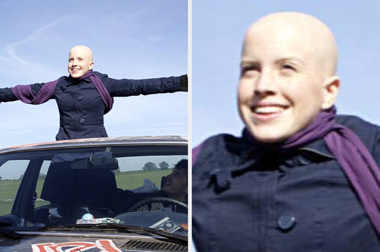Person smiling, standing through a sunroof with arms outstretched, wearing a dark jacket and scarf, in a car on an open road