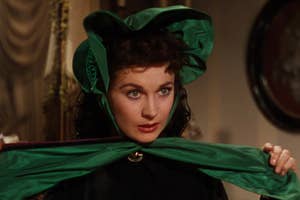 Person in vintage-style attire with a large bonnet looks intense while adjusting a matching scarf, indoors