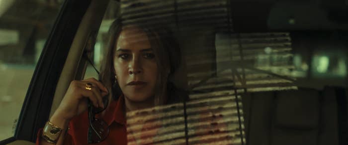 Karla Sofia Gascon sitting in a car looks out the window with a contemplative expression, holding sunglasses