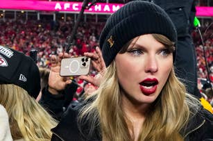 Taylor Swift in knit beanie and dark coat engaged in conversation at an event, with a crowded background