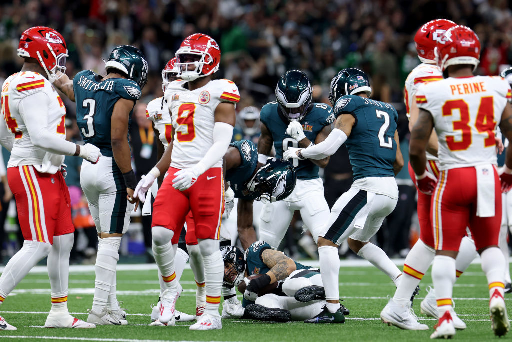 Football players from opposing teams on the field during a game, with some players interacting and others observing