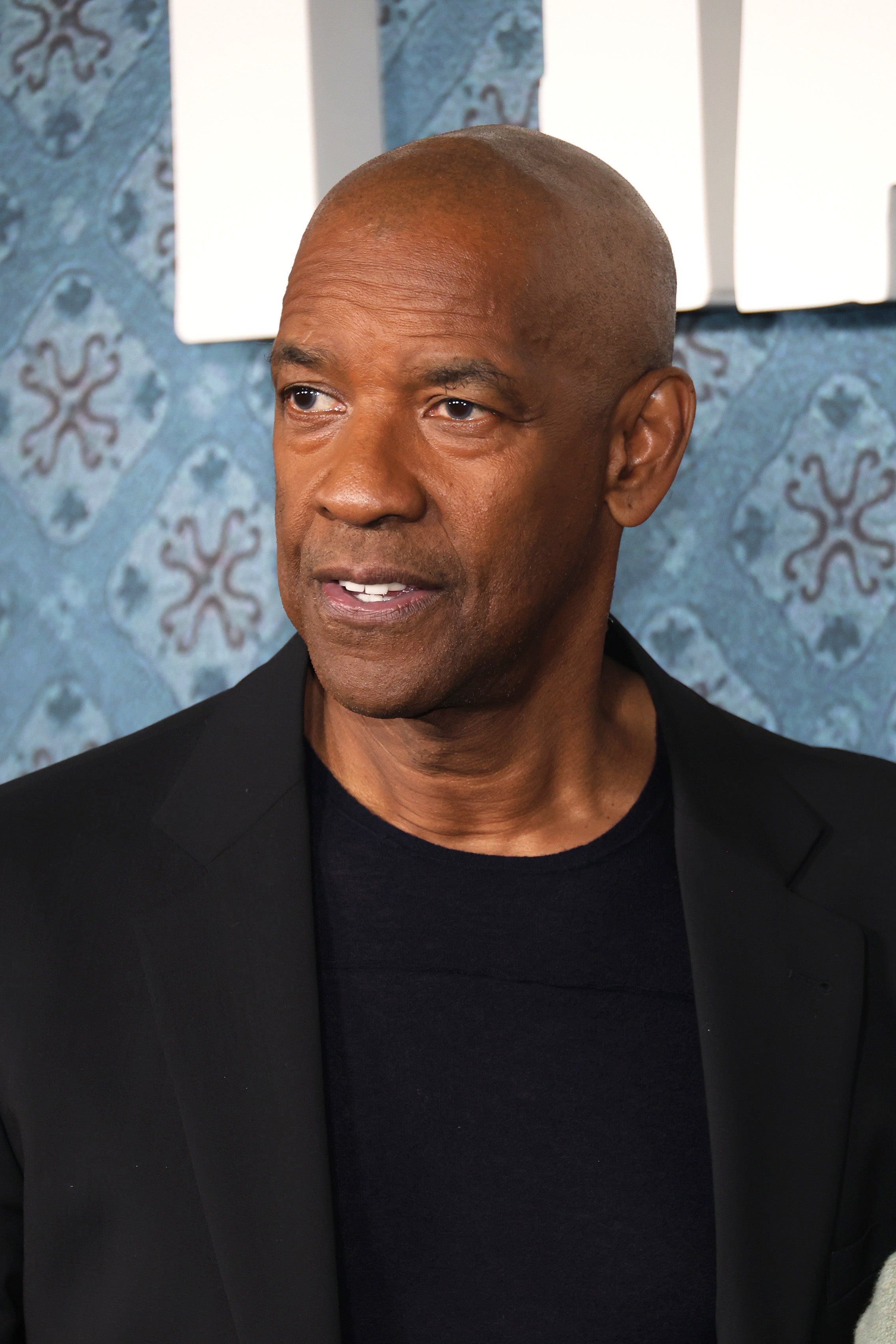 Denzel Washington on a red carpet in a black suit with a dark shirt