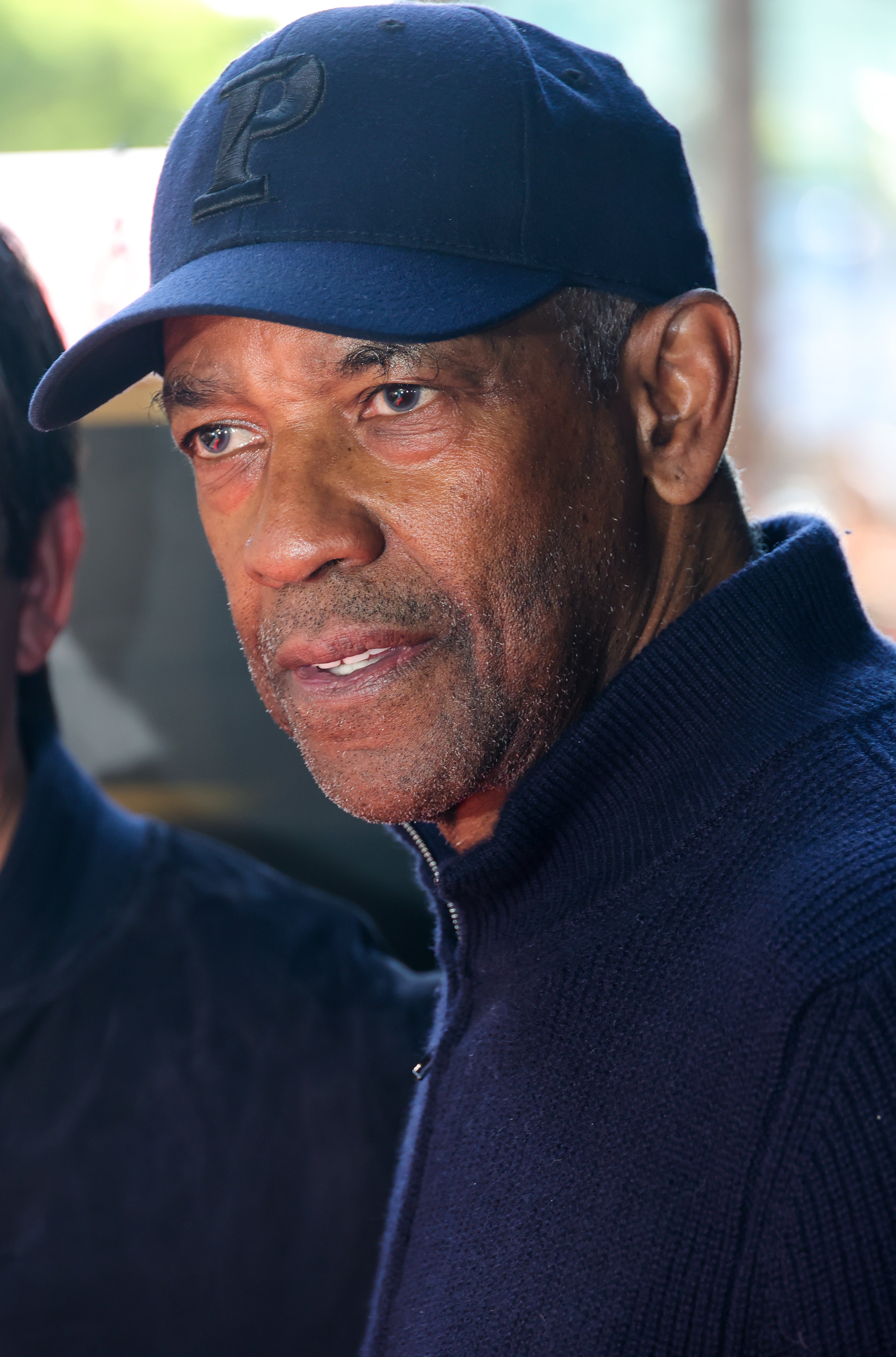 Denzel Washington wearing a navy blue cap and sweater, attending an event