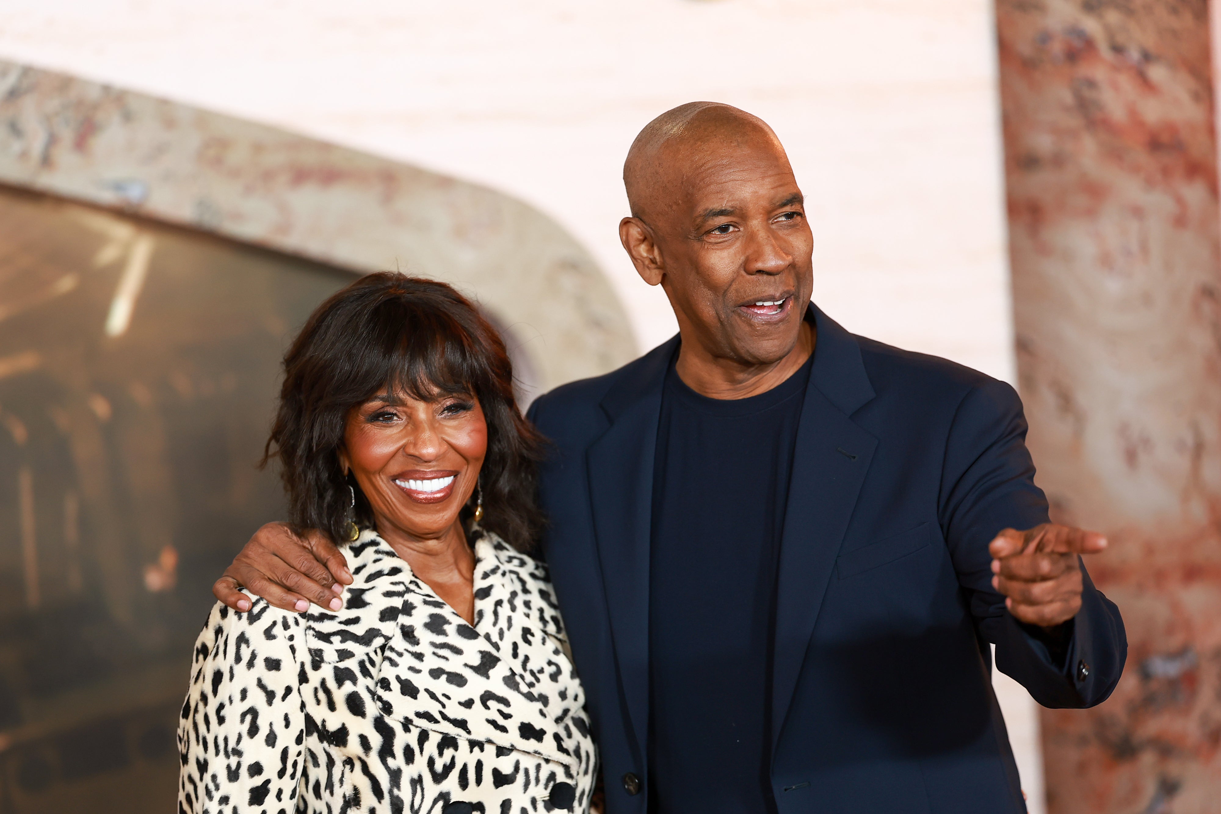 Denzel Washington and his wife Pauletta; one wears a leopard-print coat, the other a dark suit. They appear in a public event setting